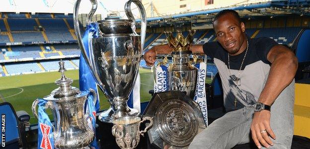 Didier Drogba poses with Chelsea's trophies at Stamford Bridge