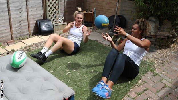 Meg Jones and Celia Quansah sit with their legs off the ground throwing a medicine ball between them