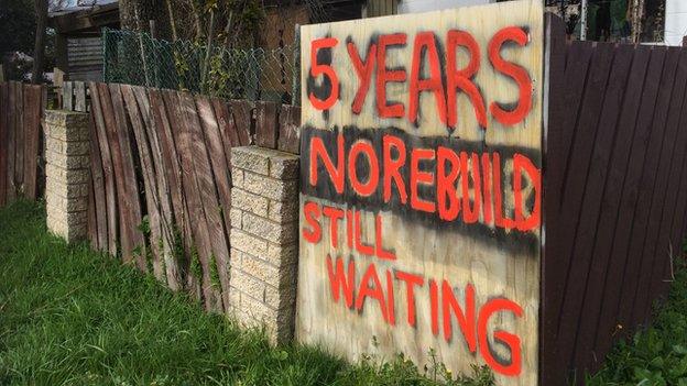 A sign outside a damaged house in Christchurch that reads '5 years, no rebuild, still waiting'