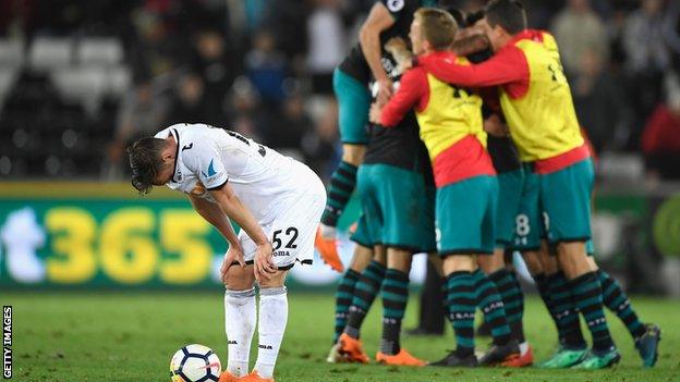 Connor Roberts bows his head in disappointment as Southampton players celebrate a season-defining victory at Swansea in May 2018