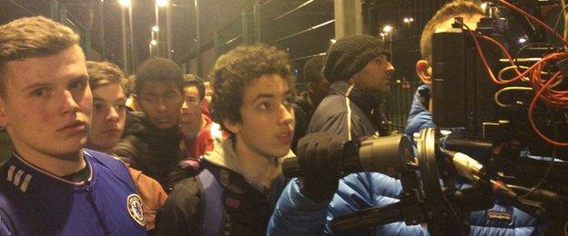 Camera crew and participants looking on at five-a-side games being played