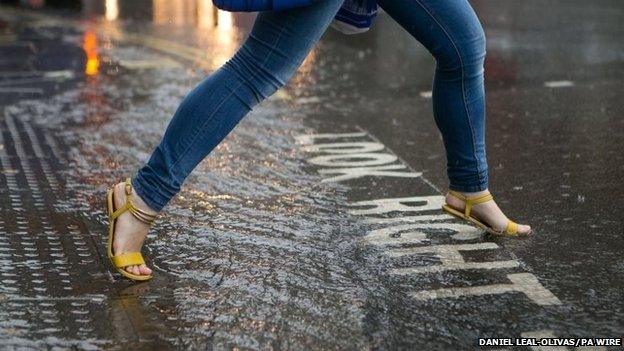 A woman steps over a large puddle