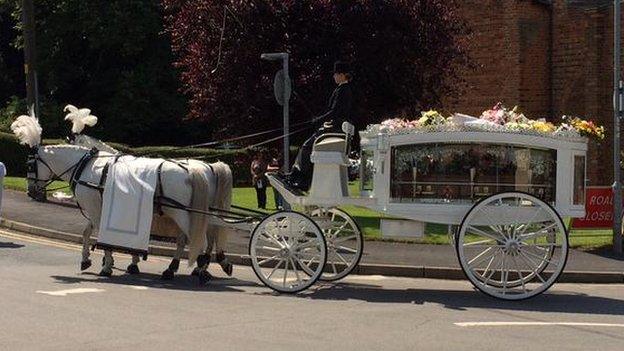 A white horse-drawn hearse carrying a coffin