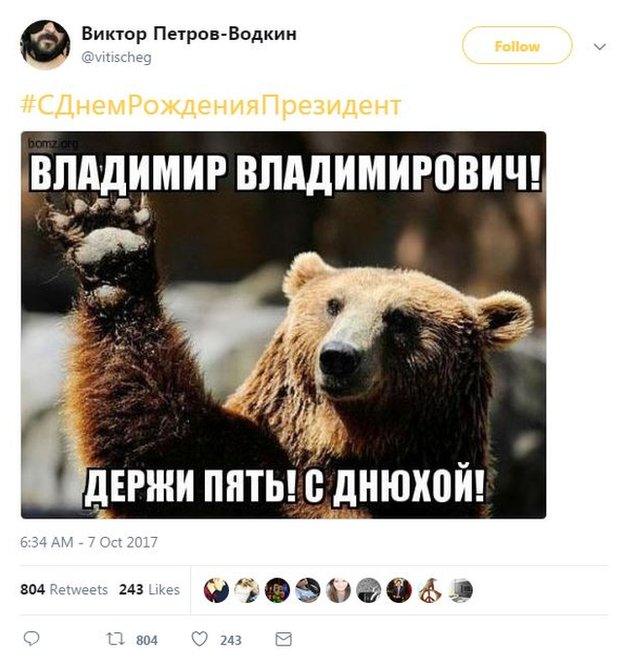 Picture of a tweet with a photo of a bear extending its paw. The hashtag translates as "Happy Birthday President", and the caption on the photo of the bear says "Vladimir Vladimirovich (Putin), High five! Happy B-day!"