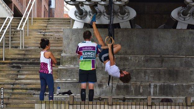 A gymnast on rings hanging under a bridge