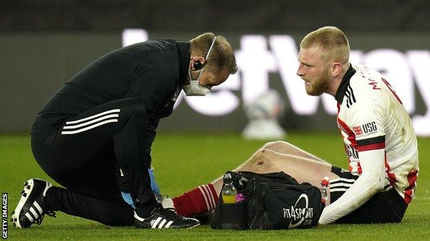 Sheffield United striker Oli McBurnie (right) receives treatment from a physio (left) for a foot injury during a Premier League game against Arsenal