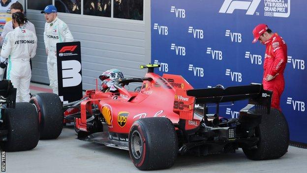 Charles Leclerc has his head down next to his Ferrari as Mercedes drivers Lewis Hamilton and Valtteri Bottas celebrate in the parc ferme