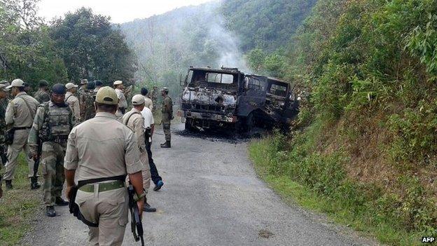 Indian security personnel stand near the smouldering vehicle wreckage at the scene of an attack on a military convoy in Chandel district, Manipur