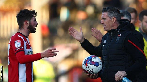 Lincoln City manager Mark Kennedy hands the ball to Lincoln City midfielder Tashan Oakley-Boothe