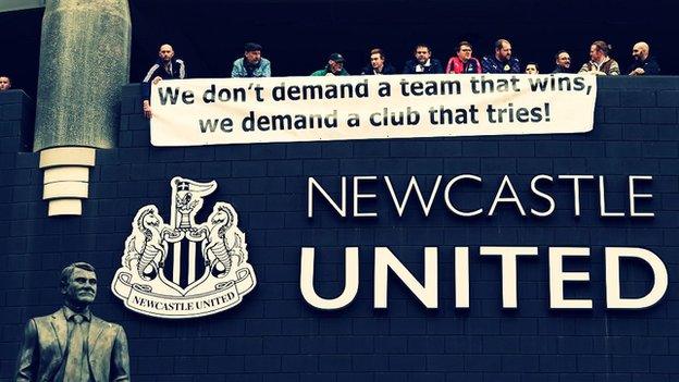 Fans hold a sign saying 'we don't demand a team that wins, we demand a club that tries'