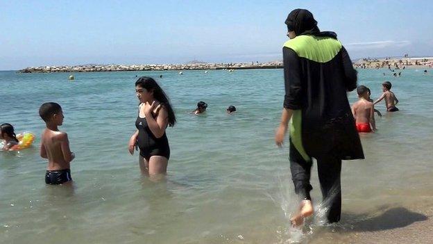 A woman wearing a full-body swimming costume walks into the water at a beach in France (file pic)