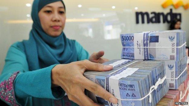 A teller at a Bank Mandiri branch handles Indonesian Rupiah currency during a transaction in Jakarta July 20, 2015