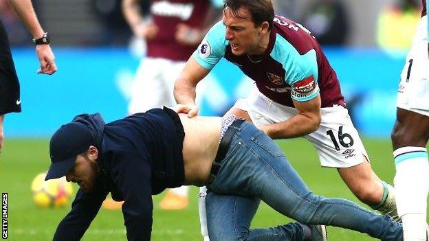 West Ham skipper Mark Noble drags a pitch invader to the floor