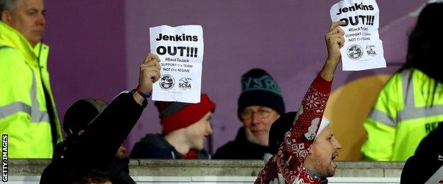 Swansea City fans hold up A4 size "Jenkins out" posters during a recent Premier League match at the Liberty Stadium