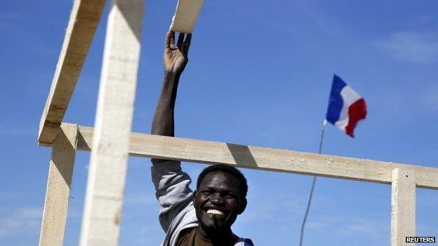 Auyob, a Sudanese migrant, smiles as he constructs a makeshift shelter at The New Jungle camp in Calais