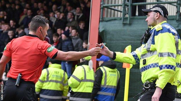 Referee Nick Walsh hands the cigarette lighter thrown on to the pitch to a policeman