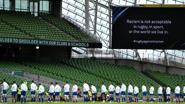 Rugby players stood in a line with the words "Racism is not acceptable in rugby, in sport, or the world we live in" on the big screen