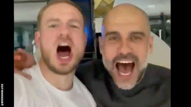 Pep Guardiola and a member of Manchester City staff sing.