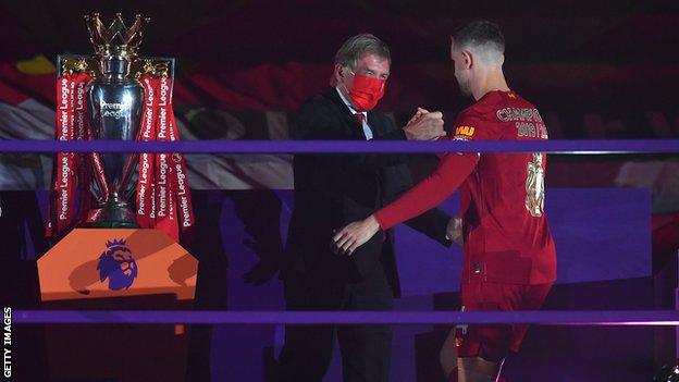 Sir Kenny Dalglish and Jordan Henderson shake hands next to the Premier League trophy