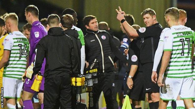 Referee Brett Huxtable orders Yeovil and Crawley players off the pitch as a drone flies over head at Huish Park