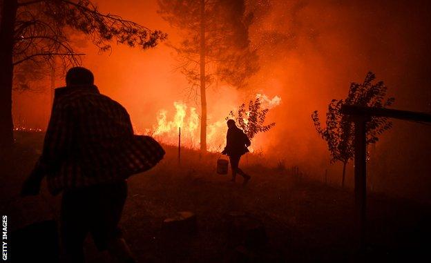 Villagers carry buckets with water to try extinguish a fire that was coming close to their houses at Amendoa in Macao, central Portugal on July 21, 2019.