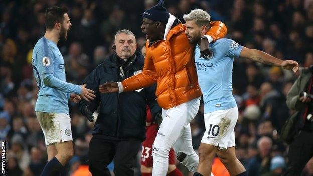 Benjamin Mendy runs on to the pitch to hug Sergio Aguero, with a steward watching on.