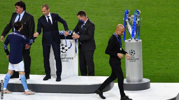 Pep Guardiola walks past the Champions League trophy