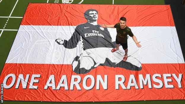 Aaron Ramsey poses on a flag which says 'One Aaron Ramsey'. The flag was made by Arsenal fans