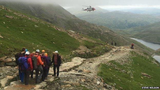 Rescuers carry a stretcher towards as a rescue helicopter hovers above