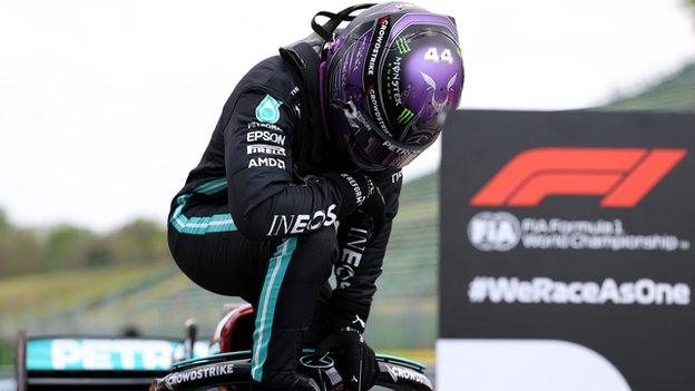 Lewis Hamilton kneels down on top of his Mercedes