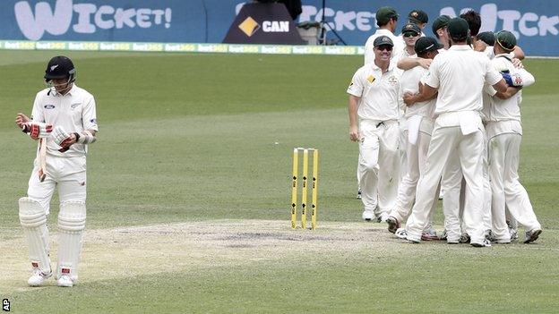 New Zealand tailender Trent Boult walks off the field as Australian players celebrate victory