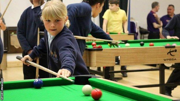 A young girl playing snooker.