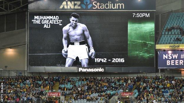 Spectators sit beneath a tribute to boxing legend Muhammad Ali before the international friendly football match between Australia and Greece in Sydney