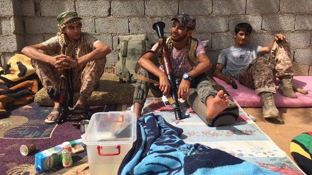 three men with weapons lounging in the sunlight, June 2016