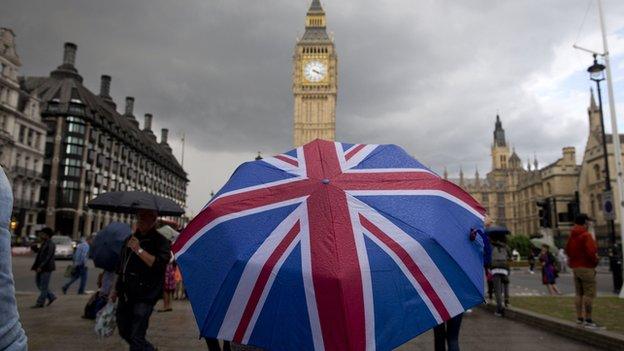 A pedestrian shelters from the rain beneath a union jack umbrella as they walk near Big Ben in London