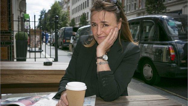 Manuela sits with a takeaway coffee