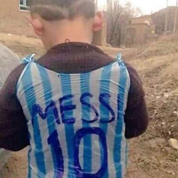 A boy wearing a Lionel Messi football shirt made out of a carrier bag