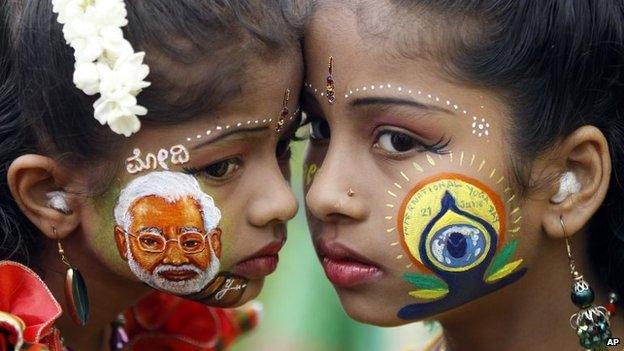 An Indian girl, left, displays a picture of Indian Prime Minister Narendra Modi painted on her face as another sports the logo of International Yoga Day in Bangalore,