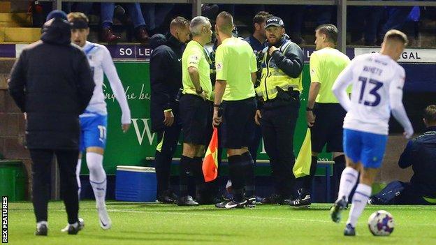 Barrow's EFL Trophy tie with Carlisle United was delayed for 17 minutes with an arrest subsequently made after the firework was thrown onto the pitch