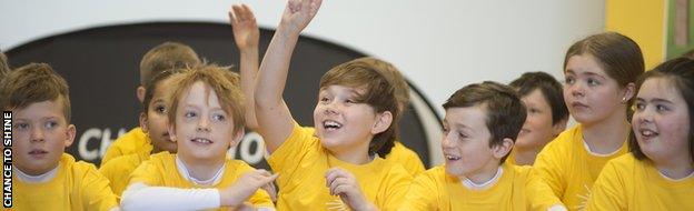 Children raise their hands to ask James Taylor questions during a Chance to Shine event