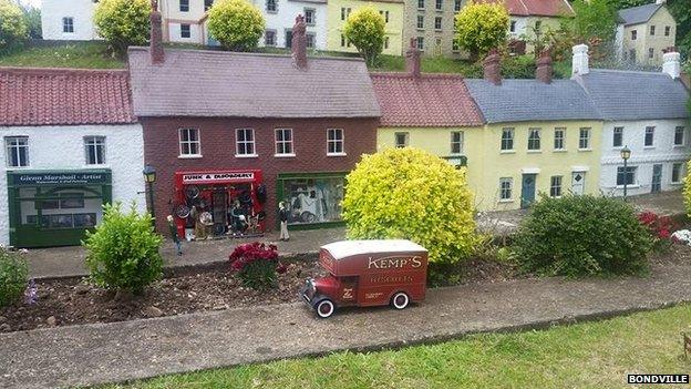 A van passes houses and shops in Bondville