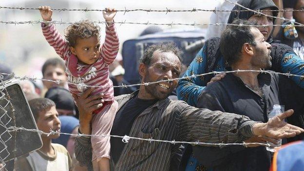 A Syrian refugee holds onto his daughter as he waits to cross into Turkey