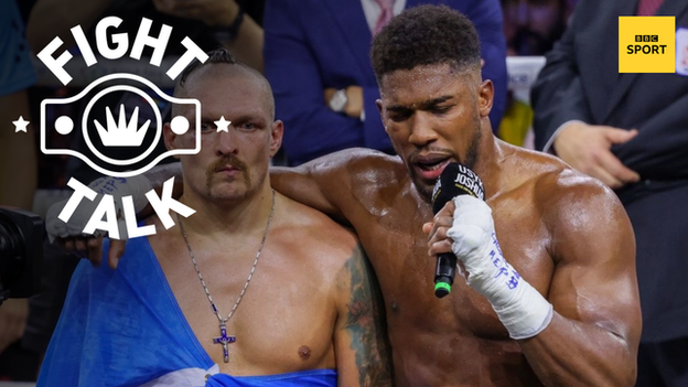 Anthony Joshua speaks on the mic with his arm around Oleksandr Usyk