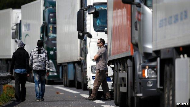 A lorry driver in Calais as two migrants walk past