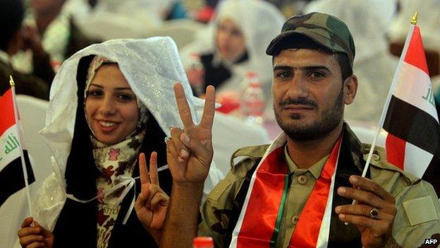 A couple make "peace" signs with their fingers while holding Iraqi flags