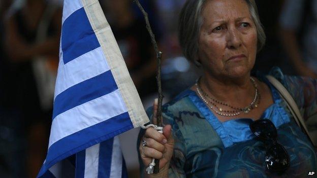 A woman holds a tree branch with a Greek flag tied on it during a rally in support to the Greek government