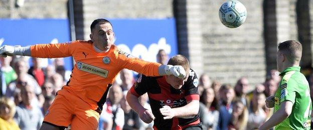 Reds keeper Brian Neeson puches clear to deny Crues striker Jordan Owens at Seaview