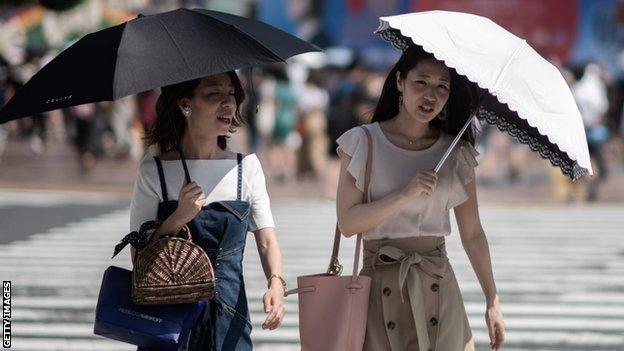 Two women use umbrellas to shield themselves from the sun in Tokyo as temperatures soar in Japan