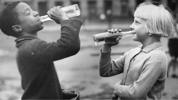 Children from Tiger Bay enjoying a drink at a day of tea and games sponsored by the Colonial Defence Association