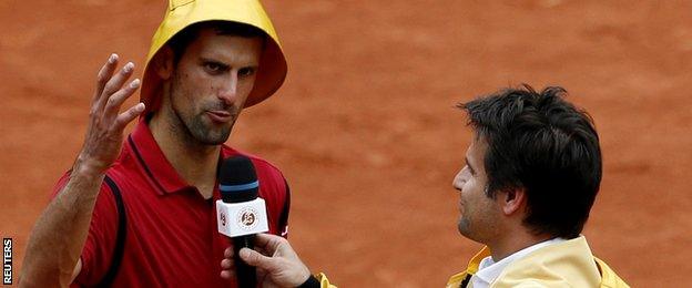 Novak Djokovic wears a rain hat as he answers to former French tennis player Fabrice Santoro